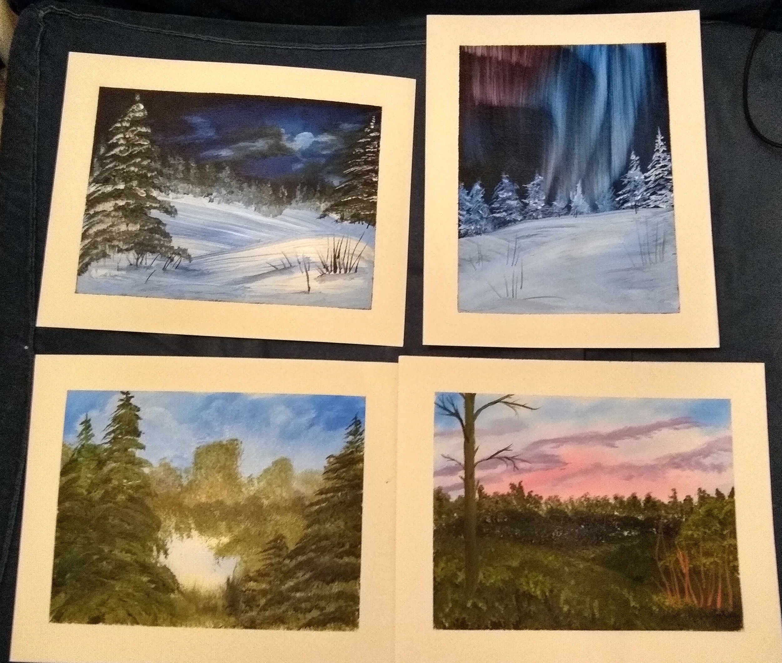 Four small paintings on paper. The top two are snowy night scenes. The bottom two are forest landscapes.