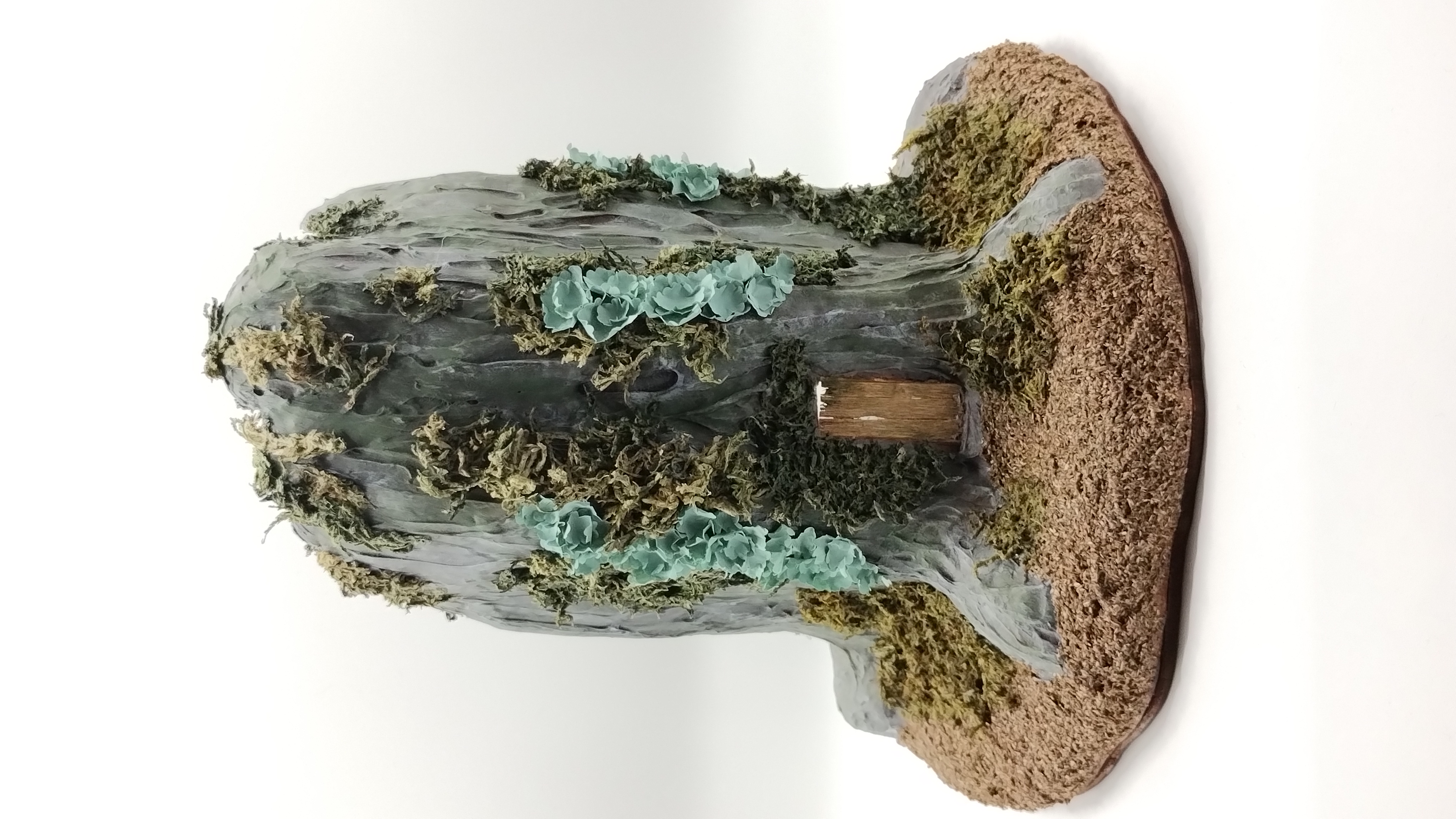 diorama of the same previous tree stump house but from the front showing a little door. the tree stump is very covered in moss and lichen