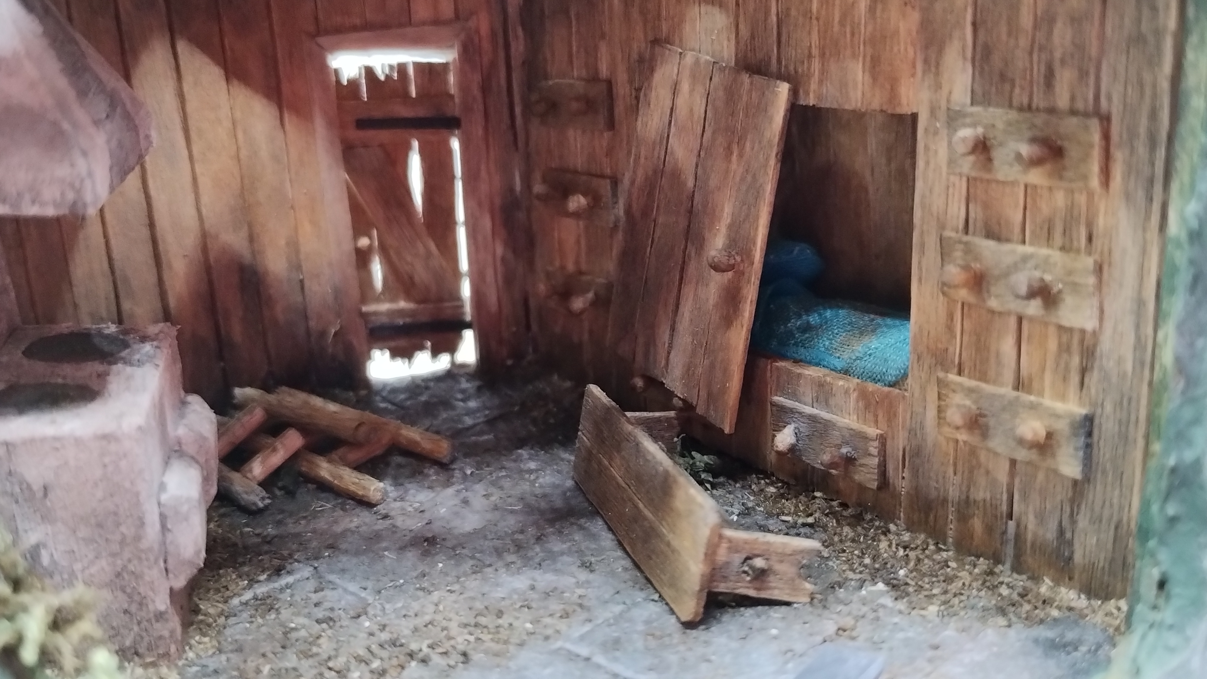 interior of tree stump house diorama. Close up showing the cupboard bed. It's strewn with dirt and one door have fallen off and is lost.