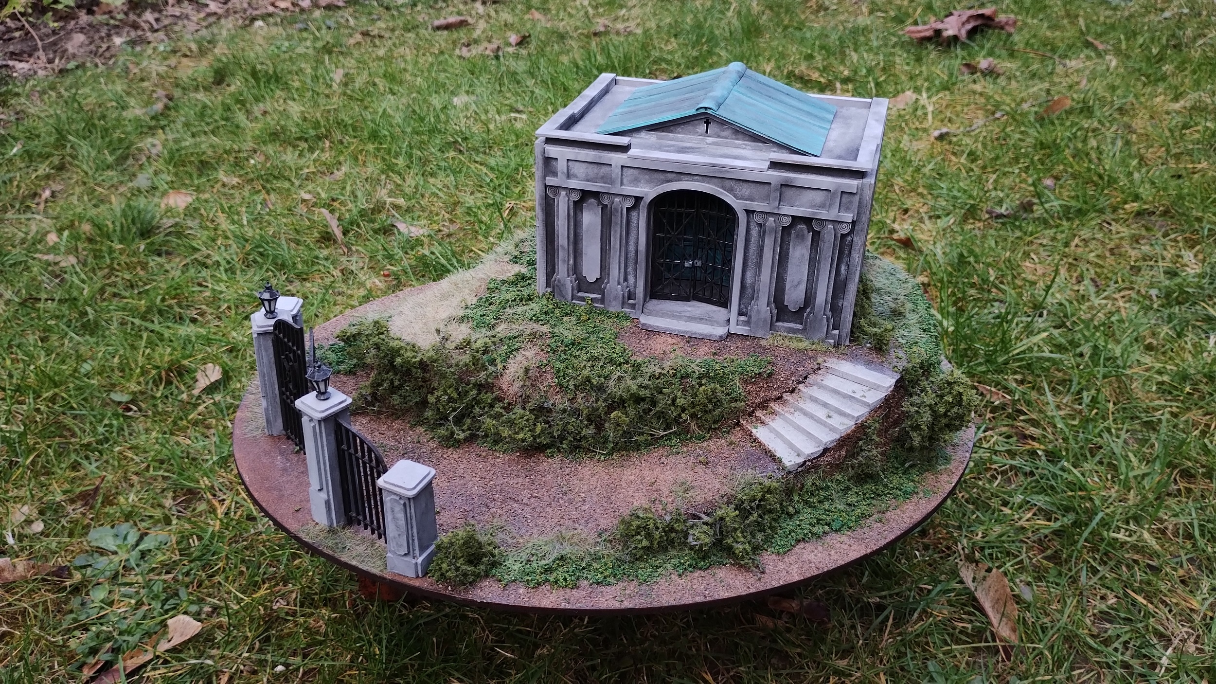 diorama of a mauseleum on a hill with a blue-green copper verdigris roof. There is some iron fencework at the bottom of the hill.